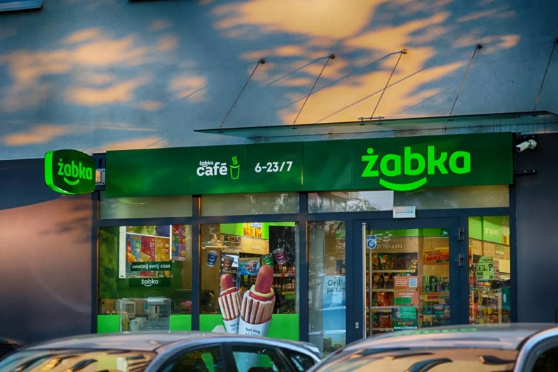 Osoba przekazująca paczkę pracownikowi sklepu Żabka, symbolizująca nadanie przesyłki kurierskiej.